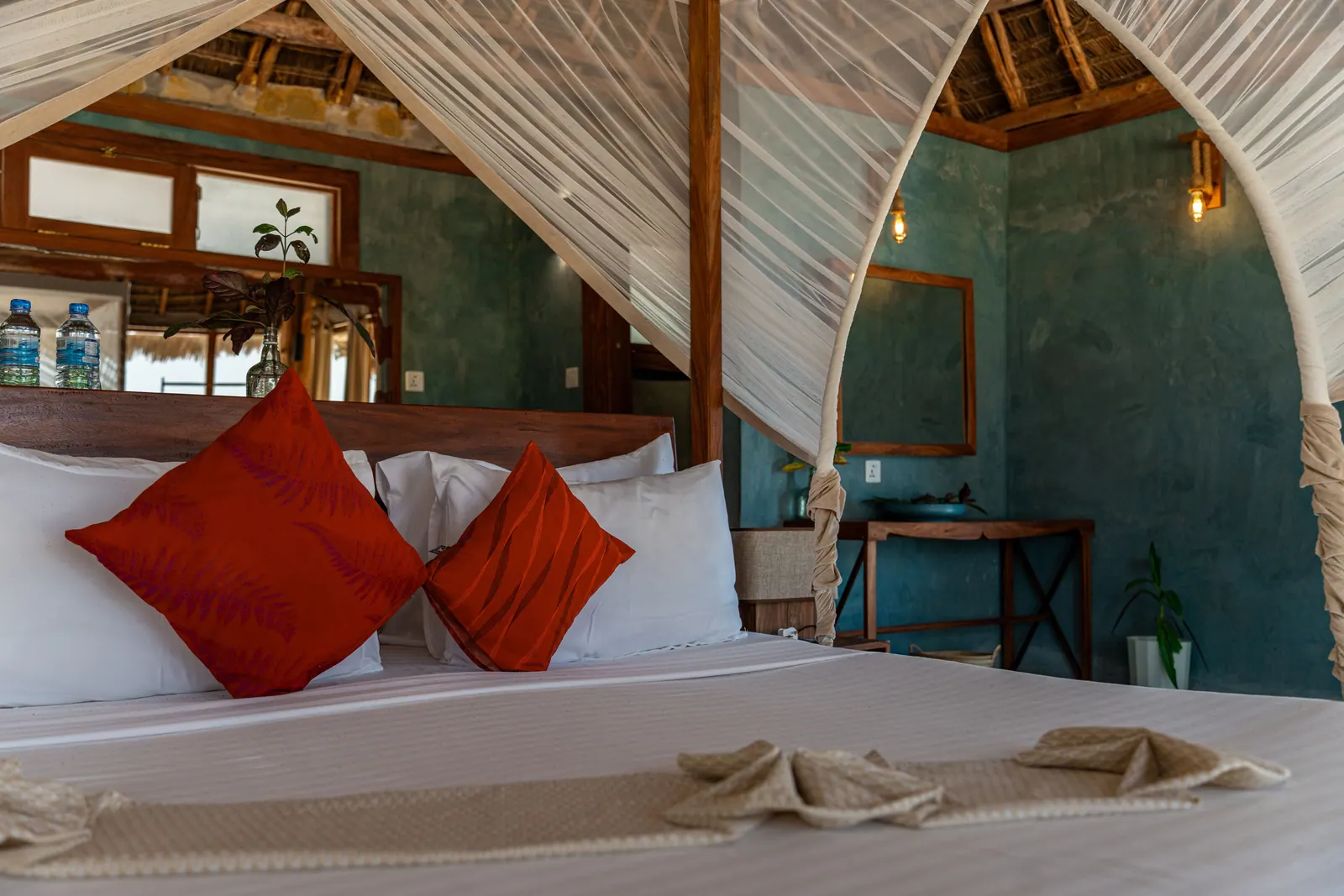 Canopy bed with orange cushions in a thatched room at Tiki Beach