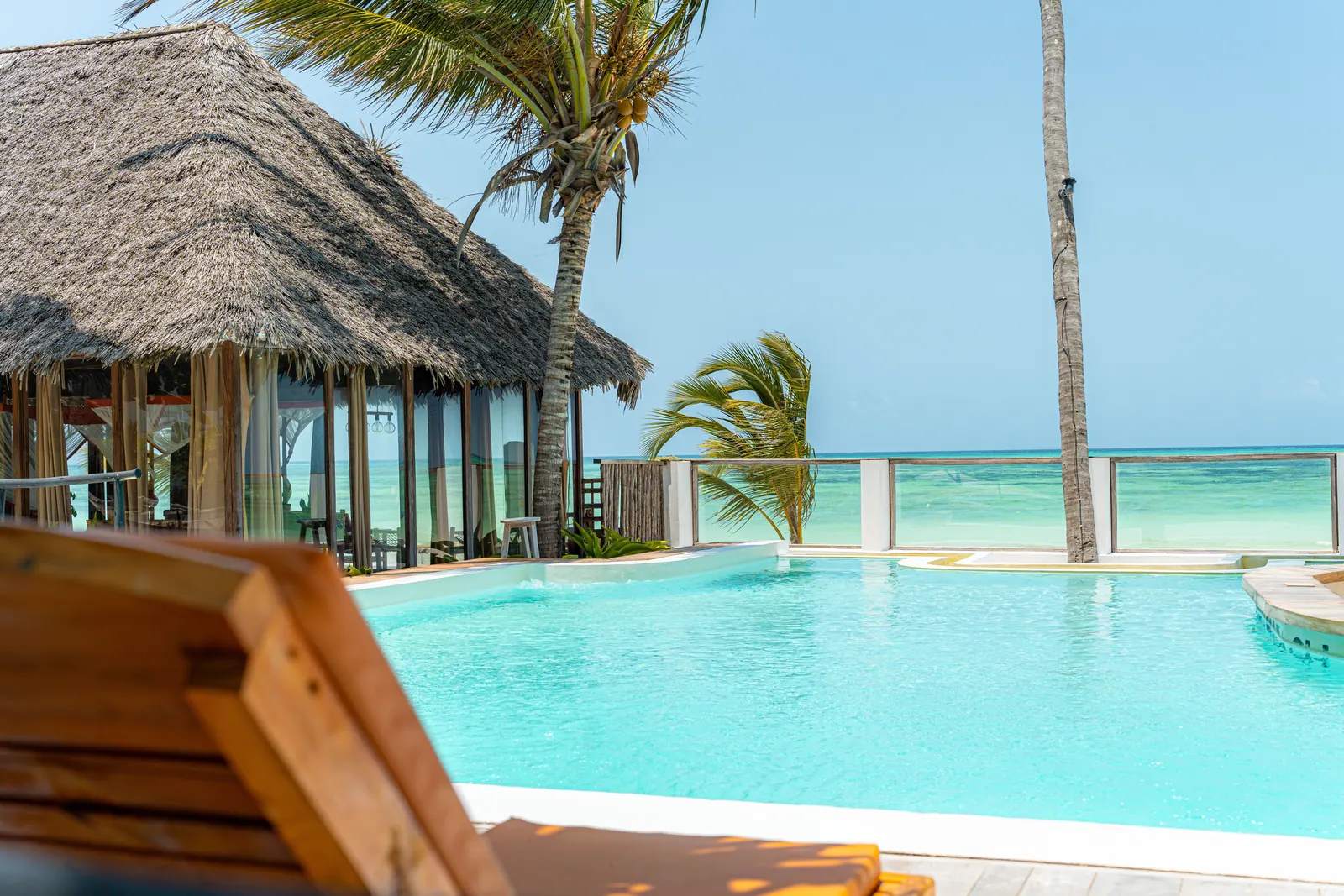 Pool at Tiki Beach with the ocean beyond, thatched roofs and palms