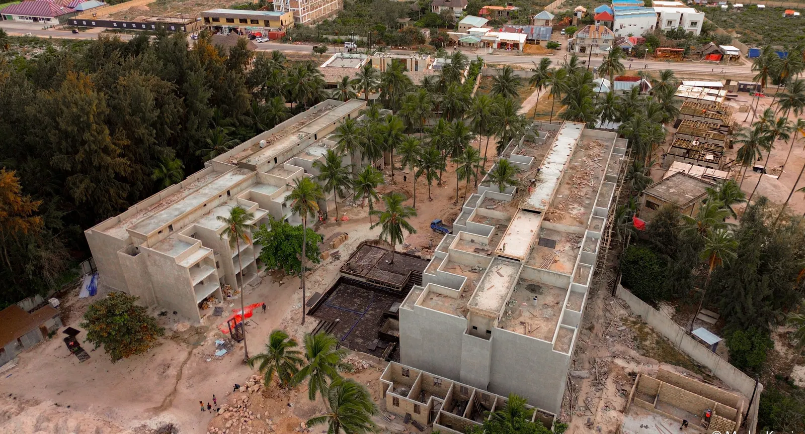 Three-storey building under construction between palms, seen from the drone